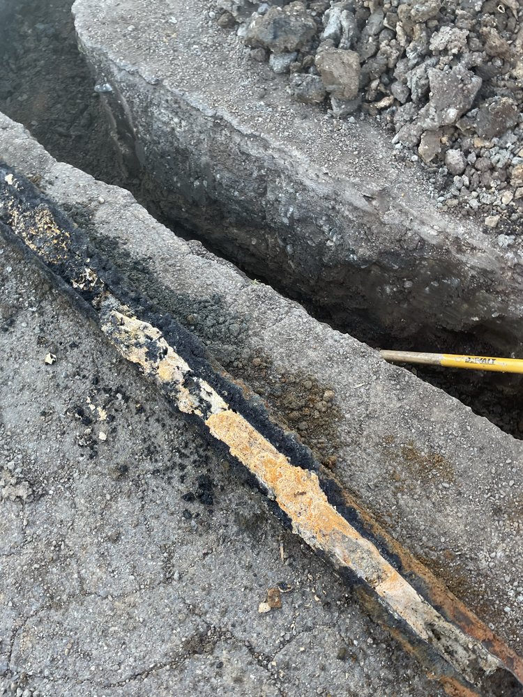Excavated trench showing a severely corroded underground main water line ready for replacement